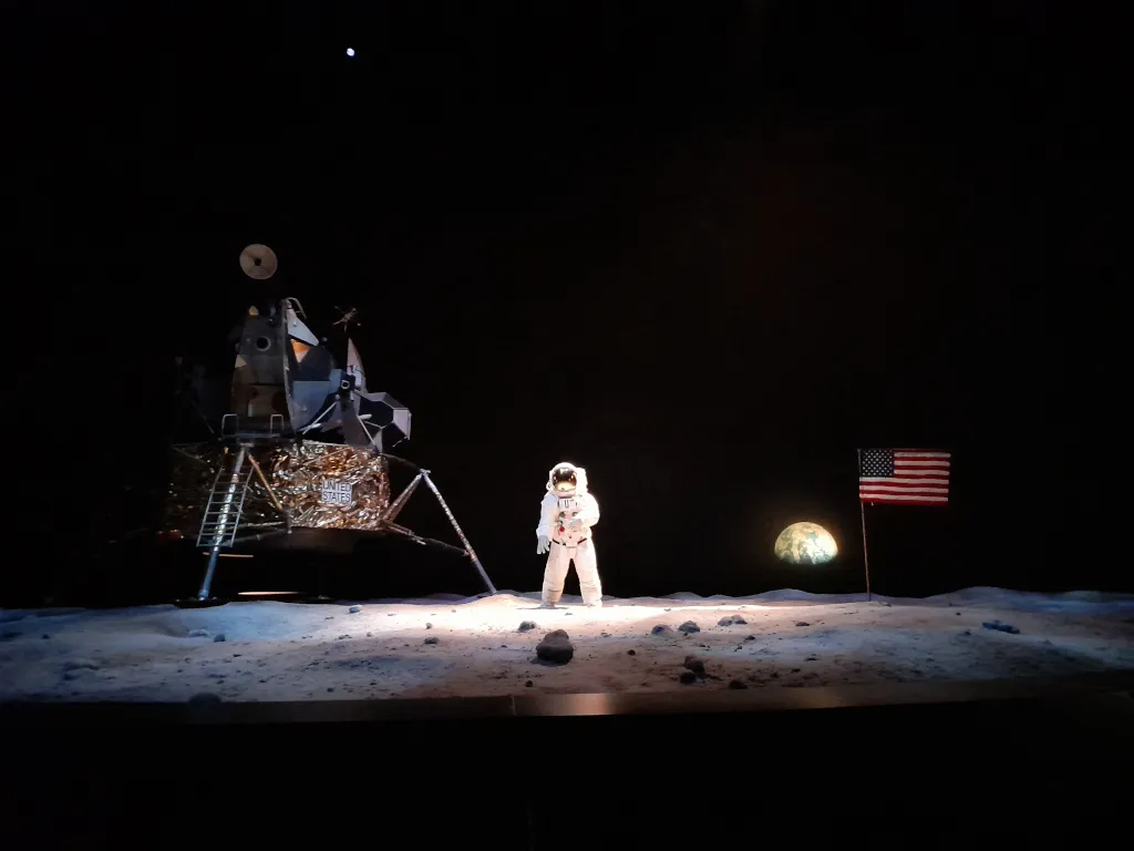 Hombre sobre la luna junto a módulo lunar y la tierra al fondo